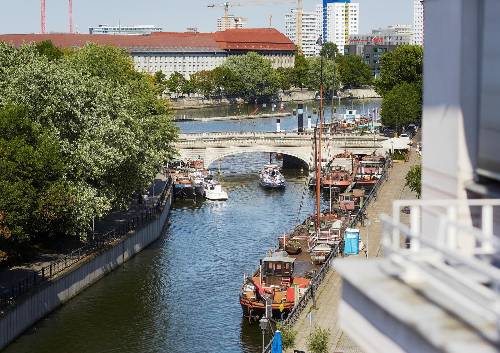 Kanal mit Booten in Berlin, sonnig, Brücke im Hintergrund, grüne Bäume.