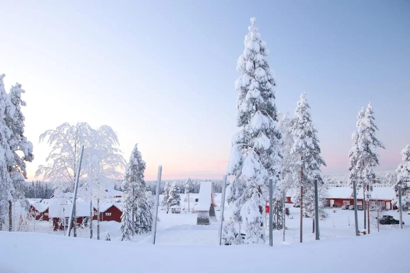 Verschneite Winterlandschaft mit roten Häusern und hohen schneebedeckten Bäumen in Lappland.