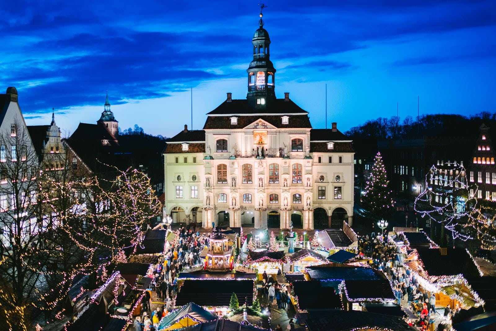 Historisches Rathaus bei Nacht, umgeben von leuchtendem Weihnachtsmarkt in Deutschland.