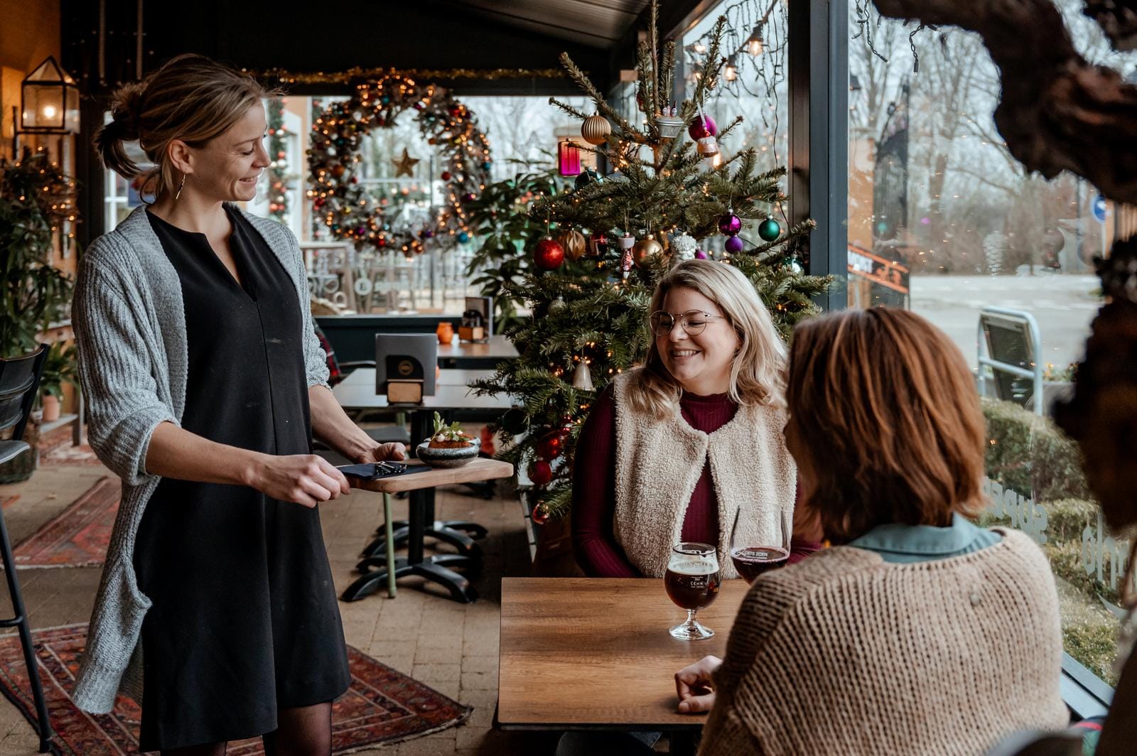 Gemütliches Café mit Weihnachtsdekoration, Tannenbaum und fröhlichen Gästen.