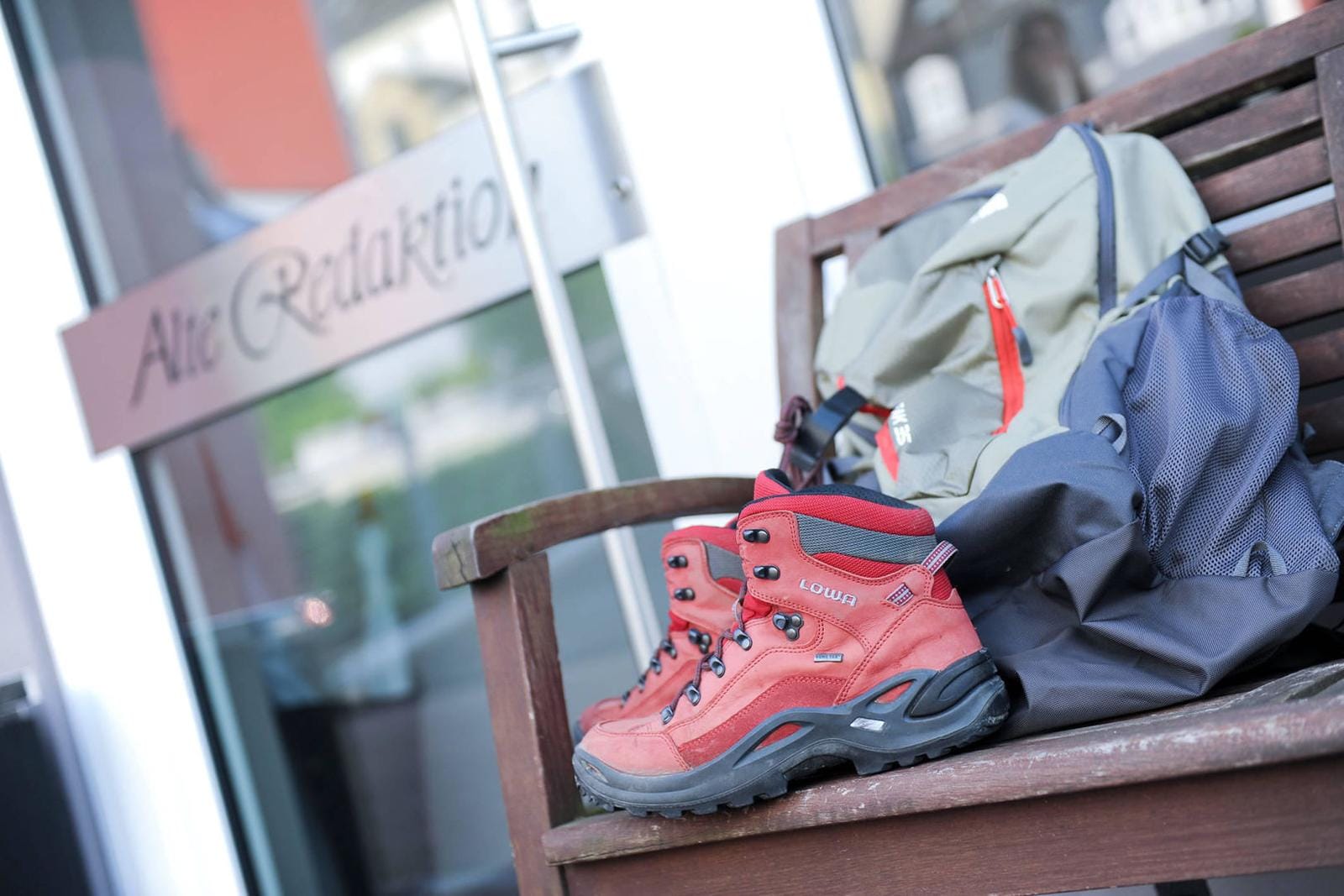 Rote Wanderschuhe und Rucksäcke auf Holzbank vor der Tür eines Gebäudes.