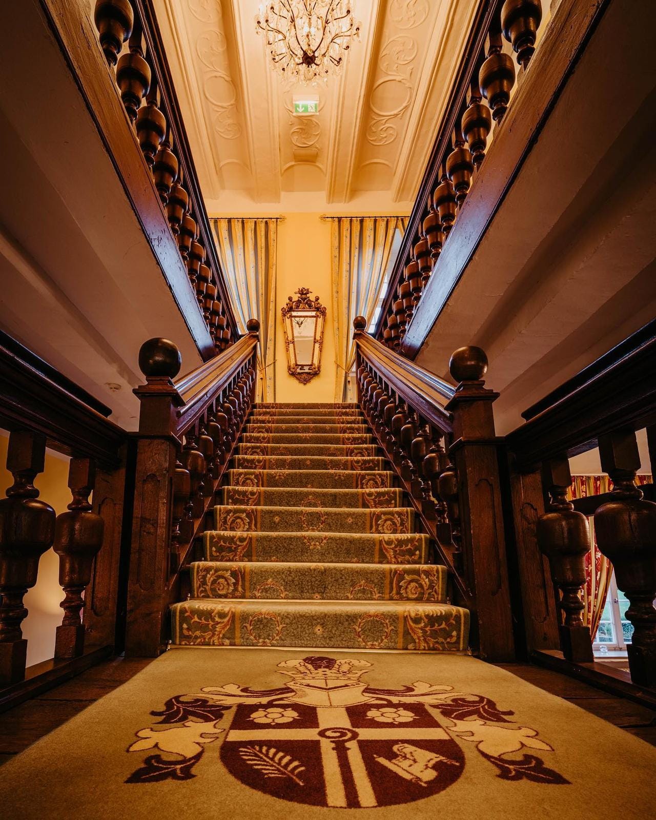 Prächtige Holztreppe mit opulentem Teppich und Kronleuchter in einem Hotel.