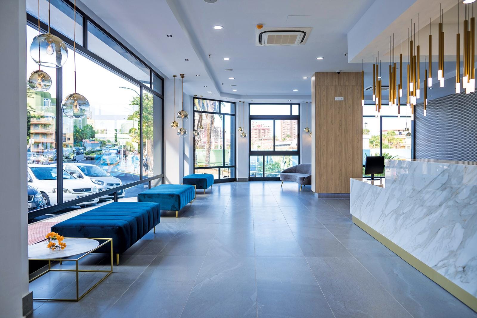 Moderne Hotel-Lobby mit blauen Samtsesseln, Marmortresen und großen Fenstern.