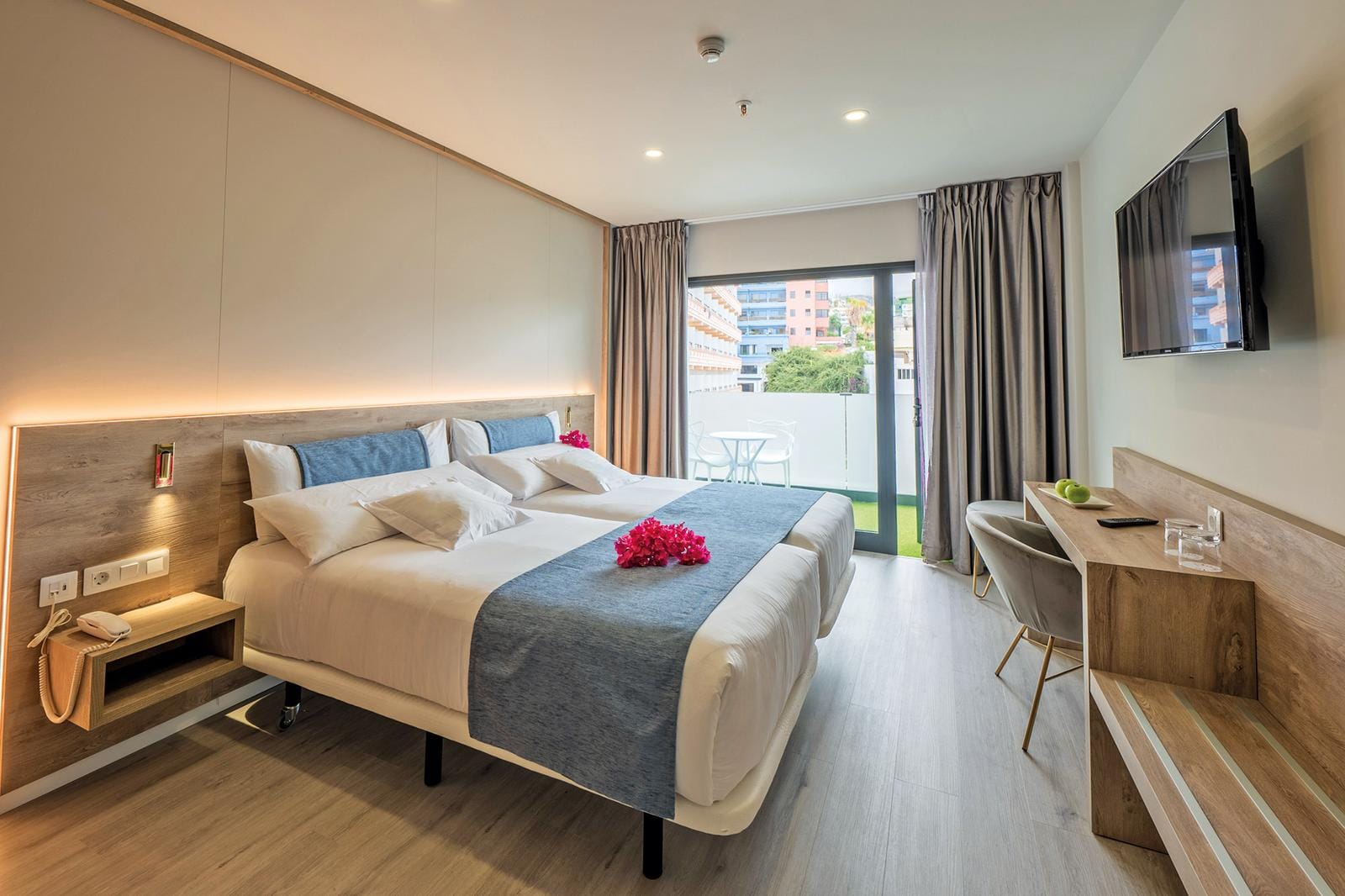 Modernes Hotelzimmer mit Doppelbett, Holzdetails, Balkon, hellen Farben und gemütlichem Ambiente.