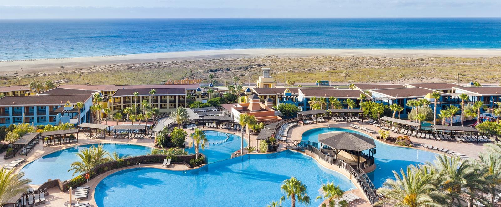 Hotelanlage am Strand mit großen Pools und Palmen, Blick auf das blaue Meer.