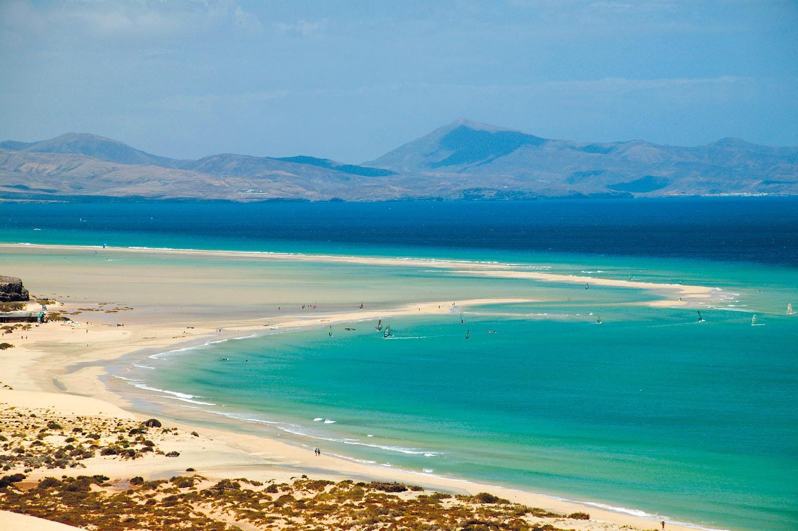Türkises Meer und Sandstrand auf Fuerteventura, Spanien, mit Bergen im Hintergrund.