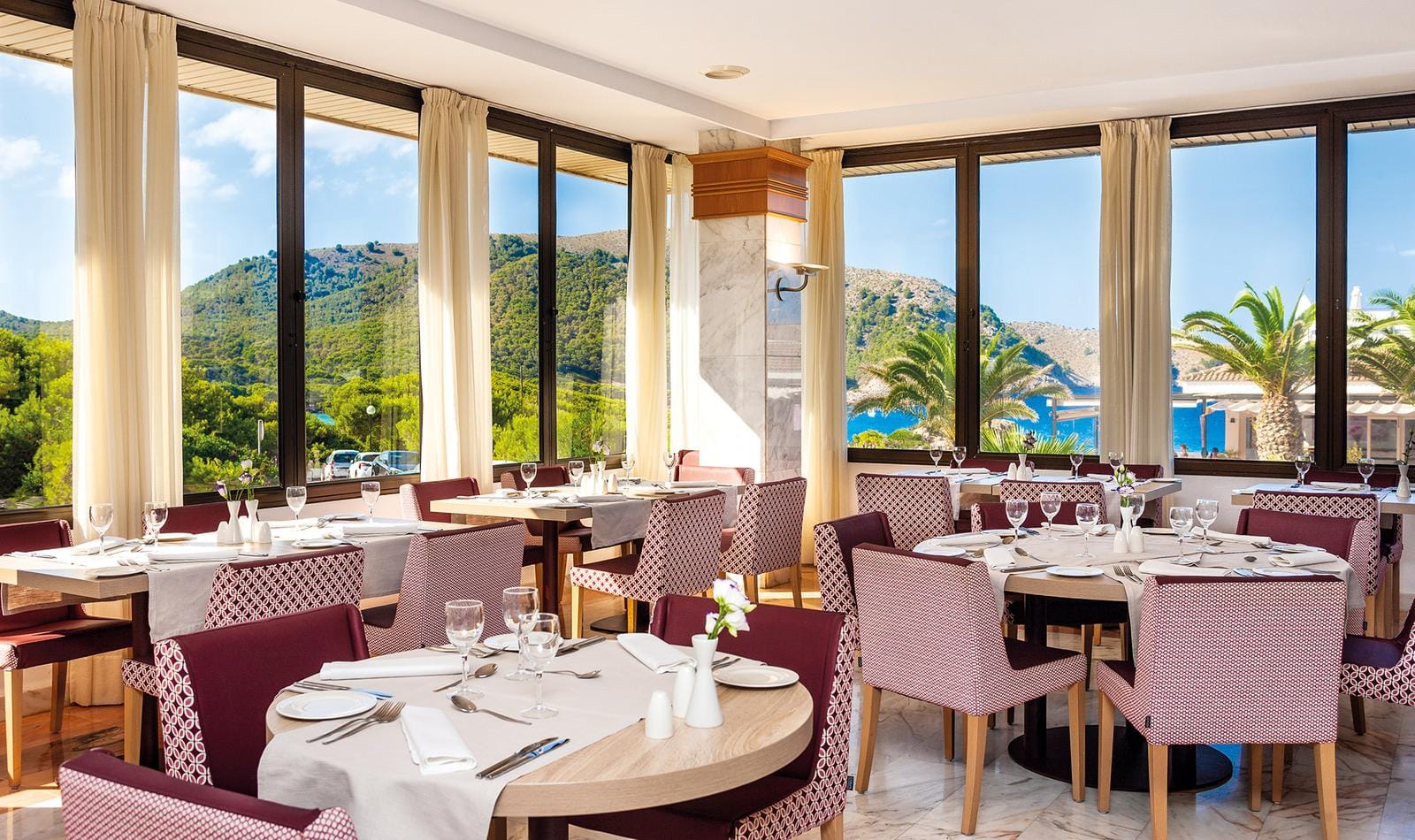 Helles Hotelrestaurant mit Panorama-Bergblick, eleganten Möbeln und weiß-roten Stühlen.