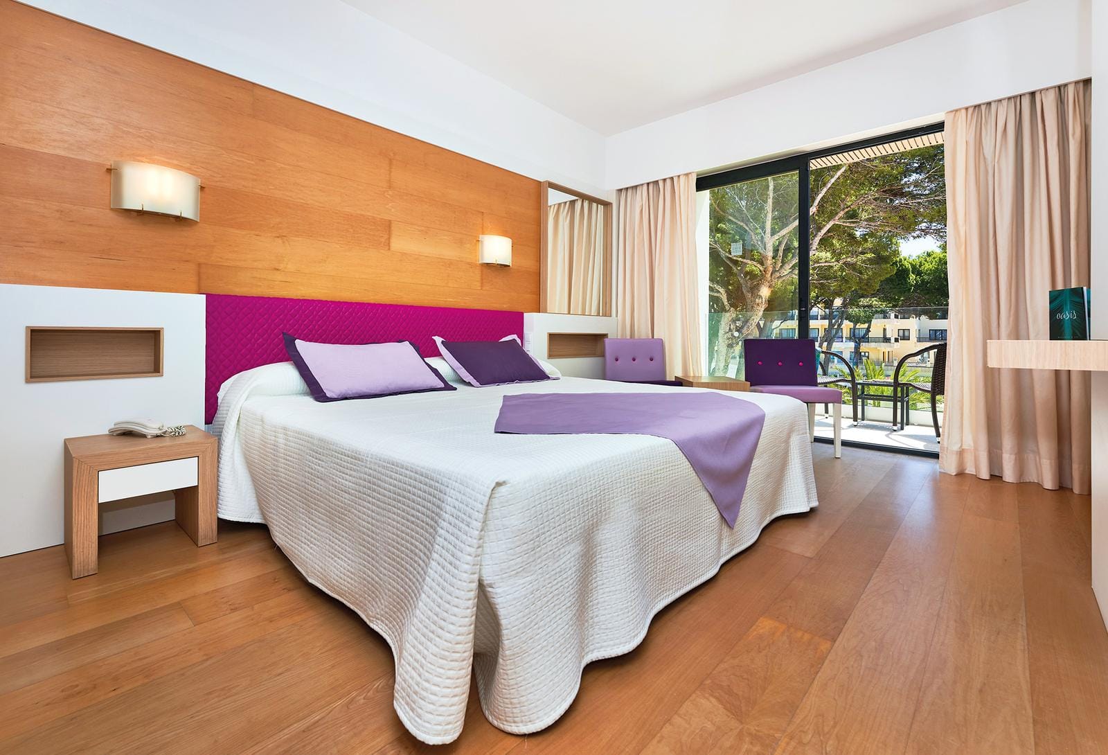 Modernes Hotelzimmer mit Holzfußboden, lila Akzenten und Balkon mit Gartenblick.