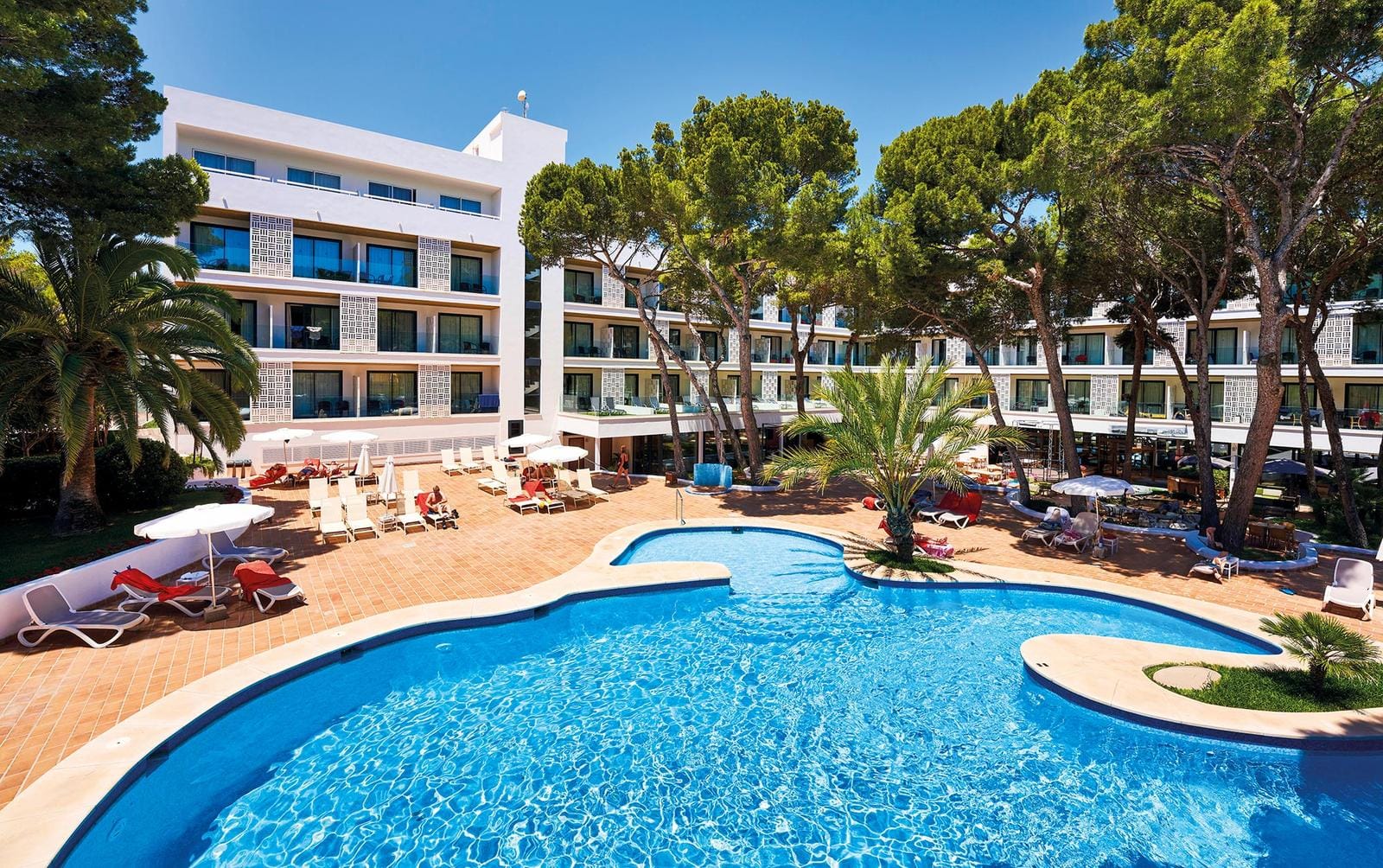 Modernes Hotel mit Pool, Palmen, Liegestühlen und weißer Fassade bei blauem Himmel.