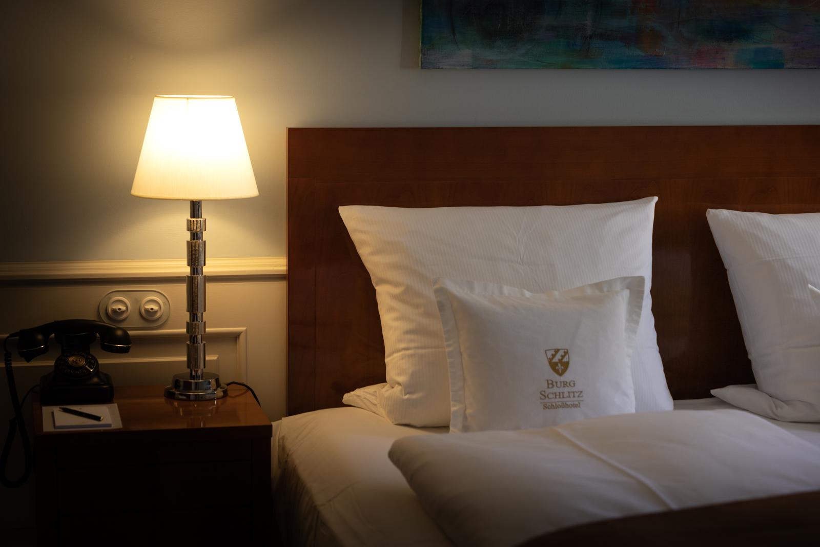 Elegantes Hotelzimmer mit Holzstuhl, Tischlampe und vintage Telefon auf Nachttisch.