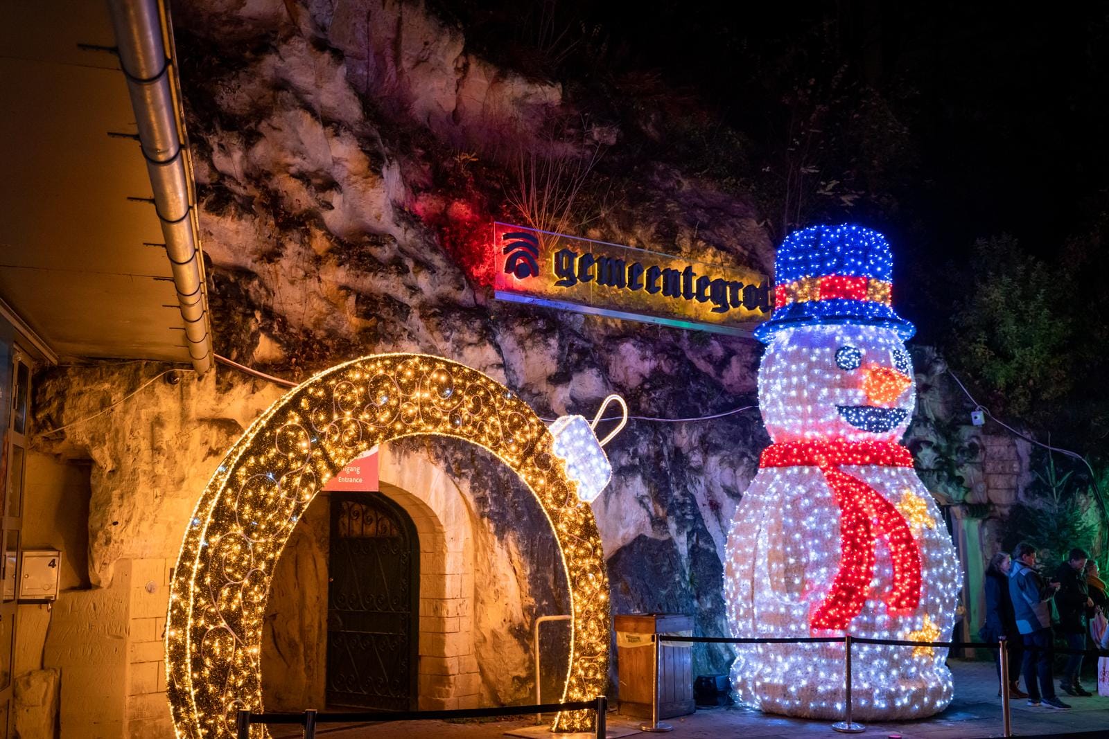 Leuchtender Schneemann und Lichterbogen vor Höhleneingang in festlicher Nachtstimmung.