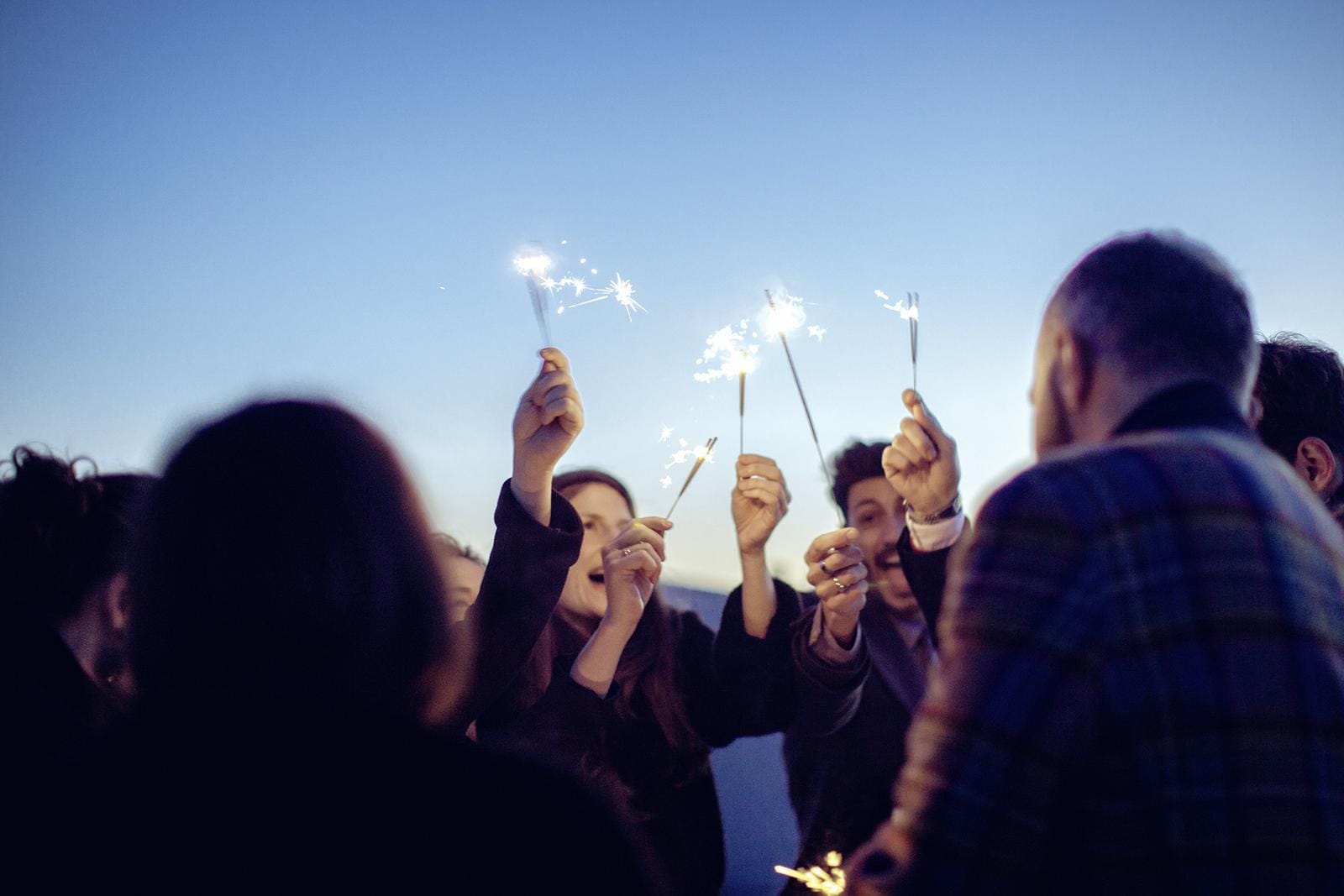 Menschen feiern mit Wunderkerzen unter klarem Abendhimmel.