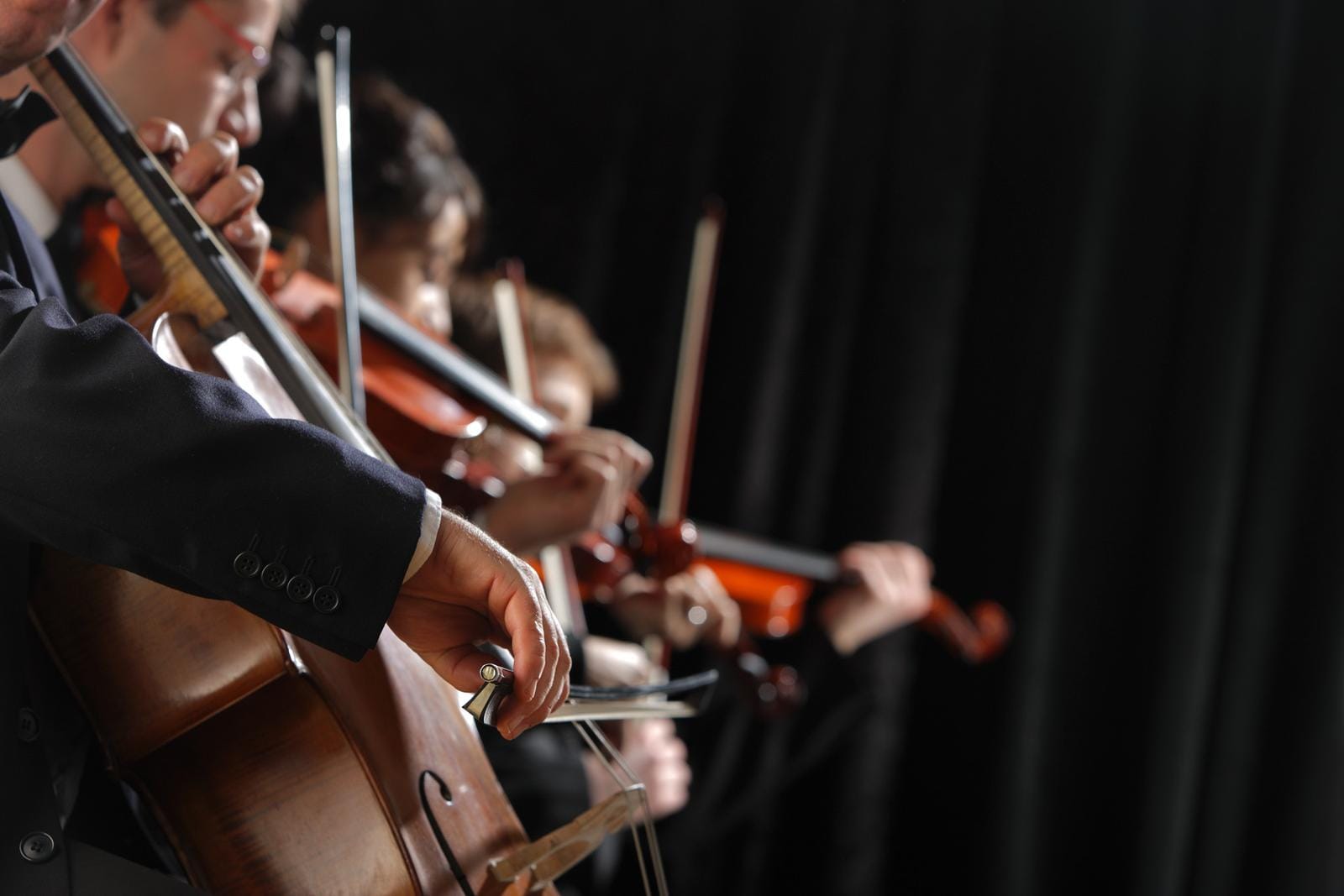 Nahaufnahme eines Orchesters, das Streichinstrumente spielt, vor schwarzem Hintergrund.