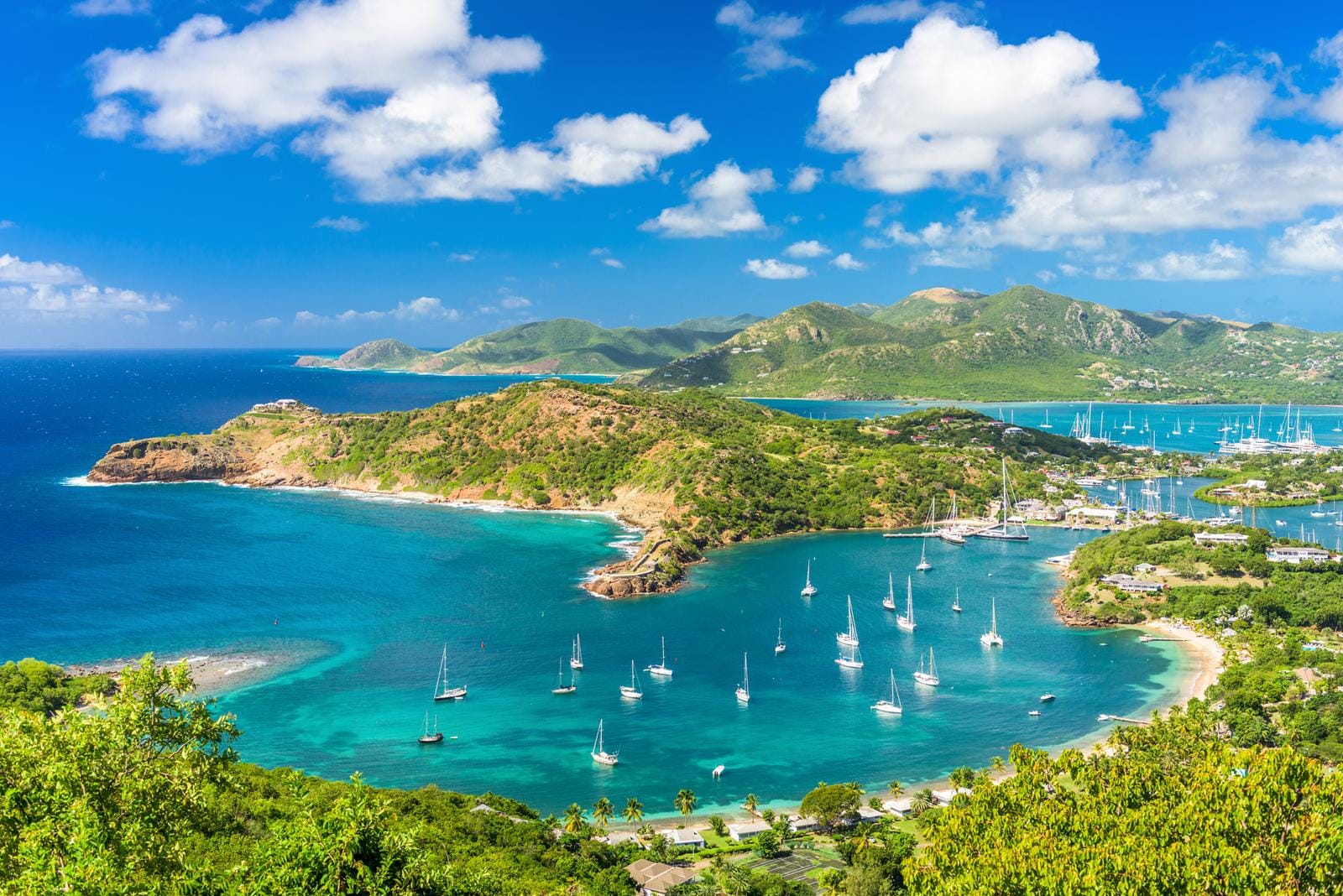 Karibikinselansicht mit Segelbooten, türkisblauem Meer und üppigen grünen Hügeln.