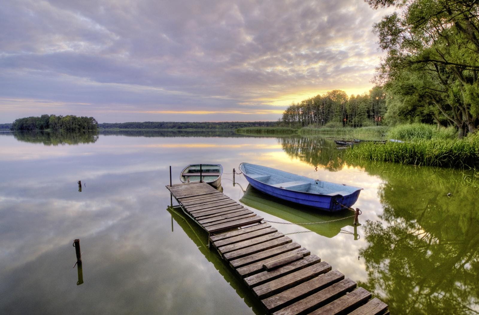 Ein ruhiger See mit Steg und Ruderboot, umgeben von Natur, lädt besonders bei Sonnenuntergang zum Entspannen ein.