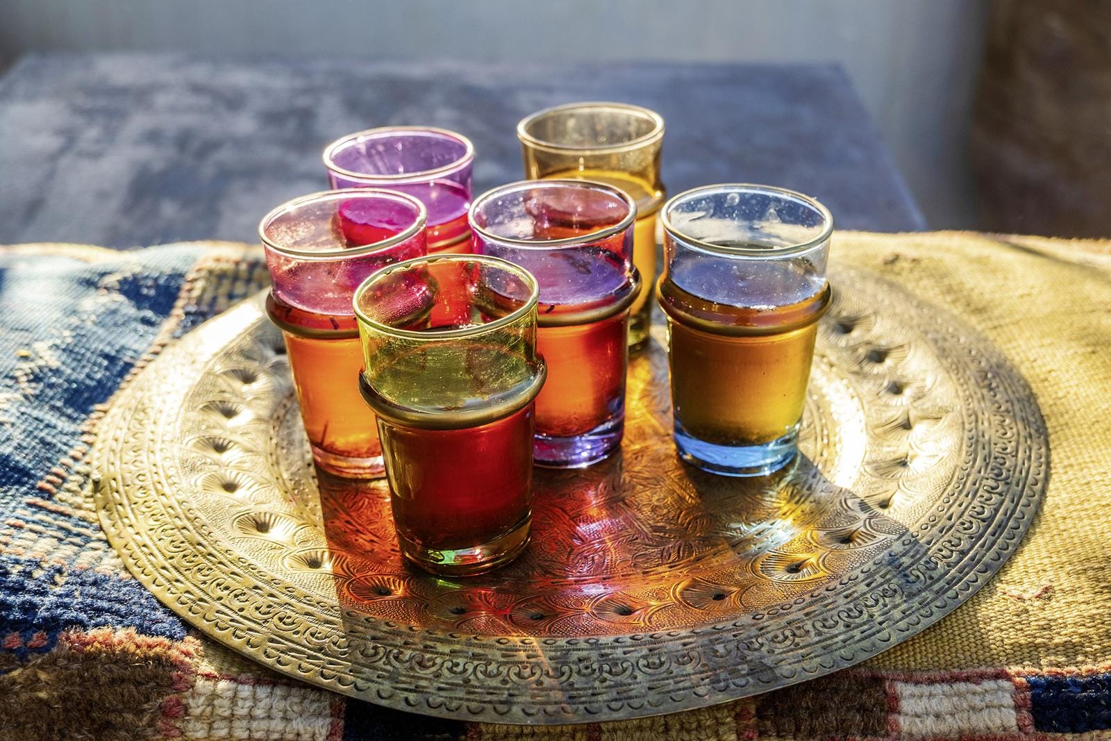 Bunte Teegläser auf graviertem Tablett, warmes Licht, orientalisches Ambiente.