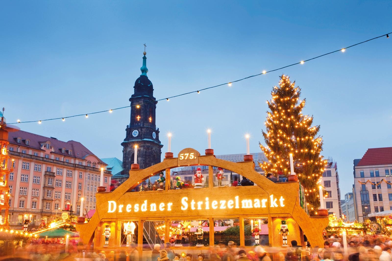 Weihnachtsmarkt in Dresden mit Kirche und beleuchtetem Tannenbaum im Abendlicht.
