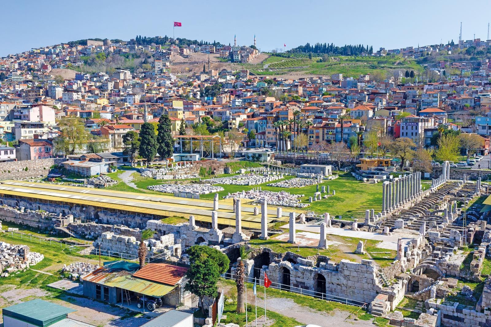 Antike Ruinen mit Säulen in Izmir, Türkei, vor einer bunten Stadtkulisse.
