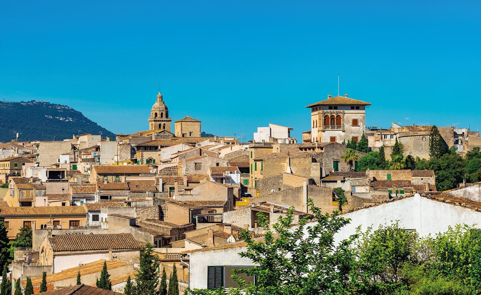 Historische Altstadt mit Ziegeldächern, Kirchturm, umgeben von grünen Hügeln, klarer Himmel.