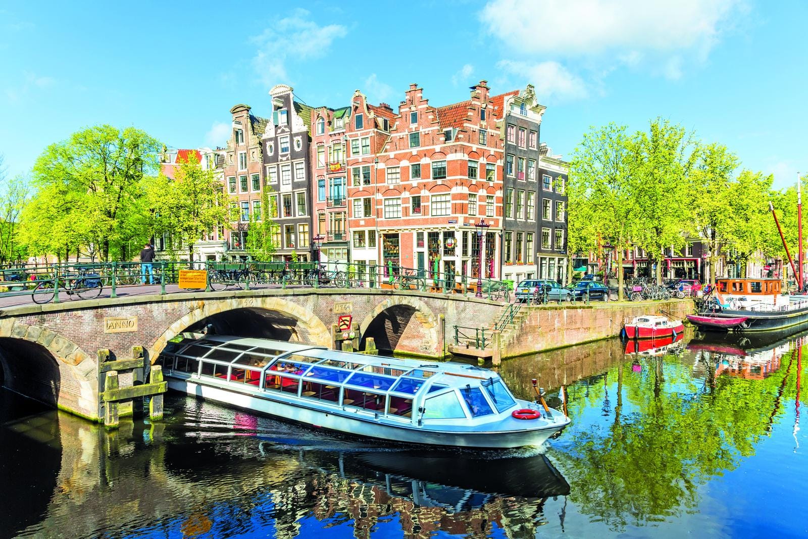 Bunte Grachtenhäuser und Touristenboot auf einem sonnigen Kanal in Amsterdam, Niederlande.