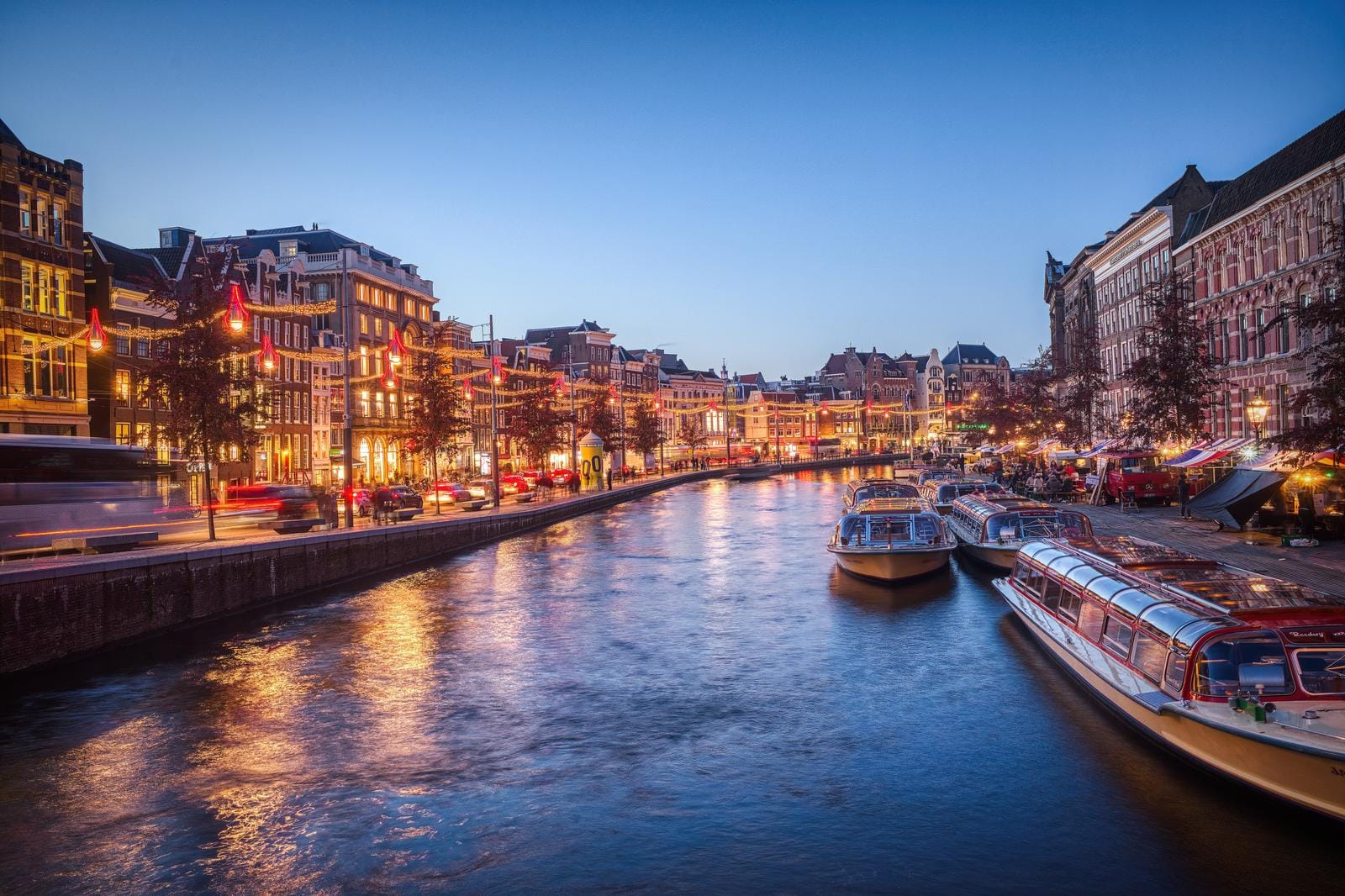 Abendliches Amsterdam mit beleuchtetem Kanal und Booten, stimmungsvolle Altstadtfassaden.