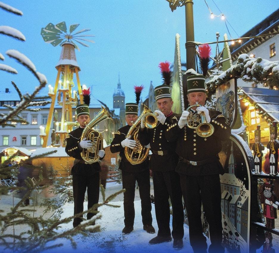 Bergmänner in Tracht spielen Blechblasinstrumente auf einem verschneiten Weihnachtsmarkt.