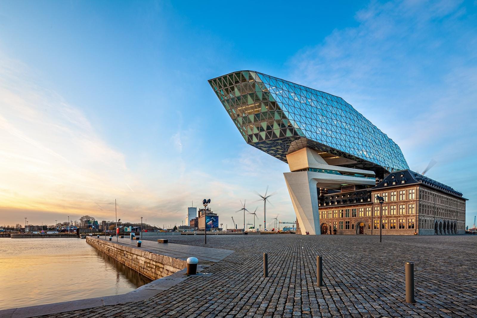 Futuristisches Gebäude mit Glasfassade am Hafen von Antwerpen bei Sonnenuntergang.