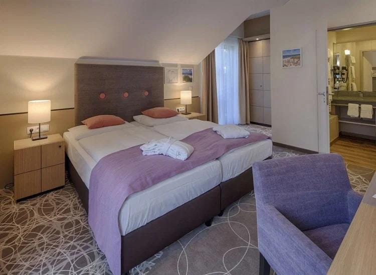 Gemütliches Hotelzimmer mit Doppelbett, lila Dekor, modernem Bad und Balkonzugang.