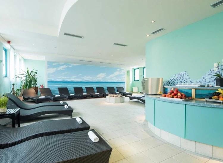 Helles Spa mit Strandmotiv, Liegestühlen, Pflanzen und Obstbuffet.