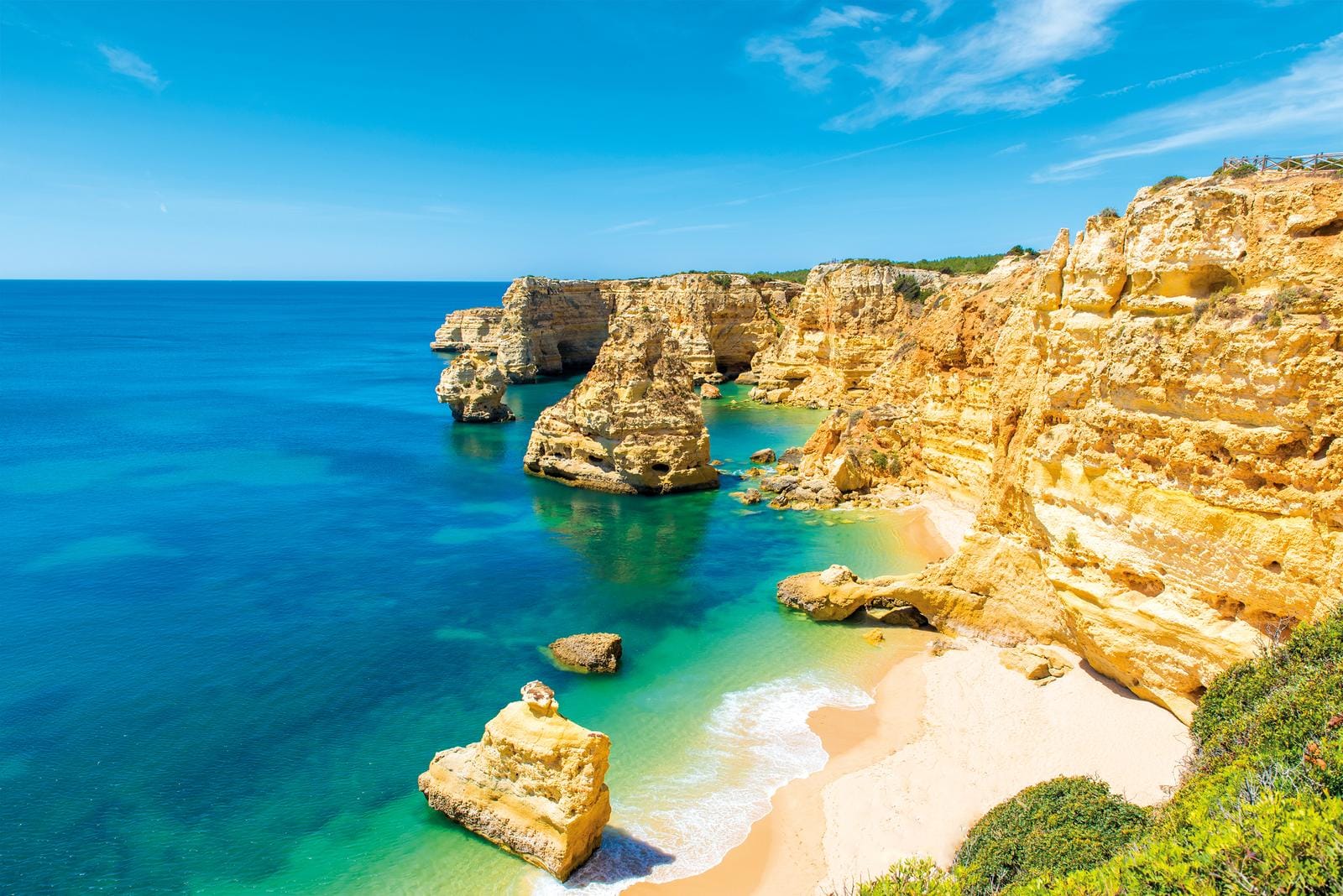 Strandbild in der Algarve, Portugal: Goldene Klippen, türkisblaues Meer und sonniger Himmel.