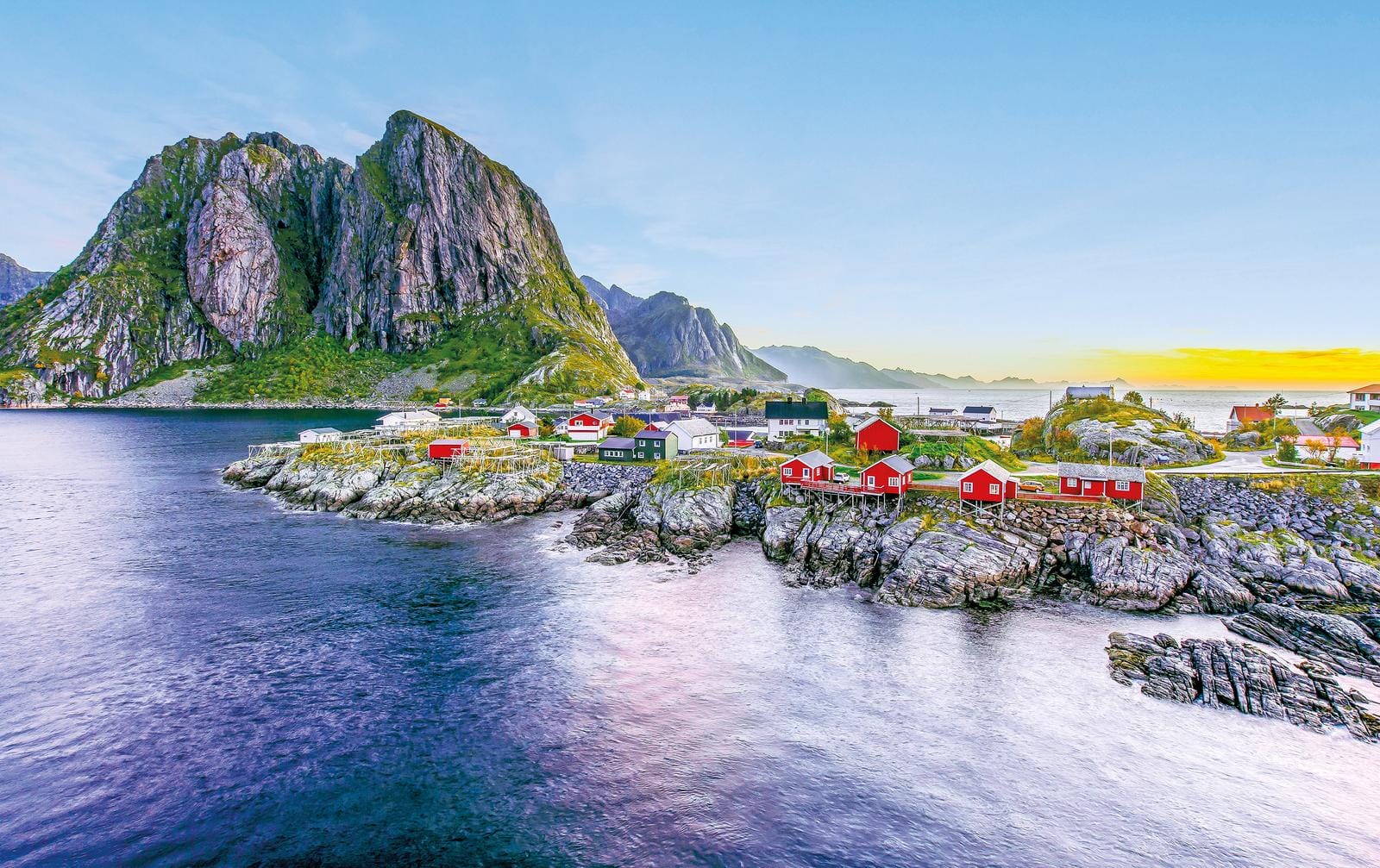 Bunte Häuser am Wasser, Norwegen, vor dramatischer Bergkulisse im Sonnenaufgang.