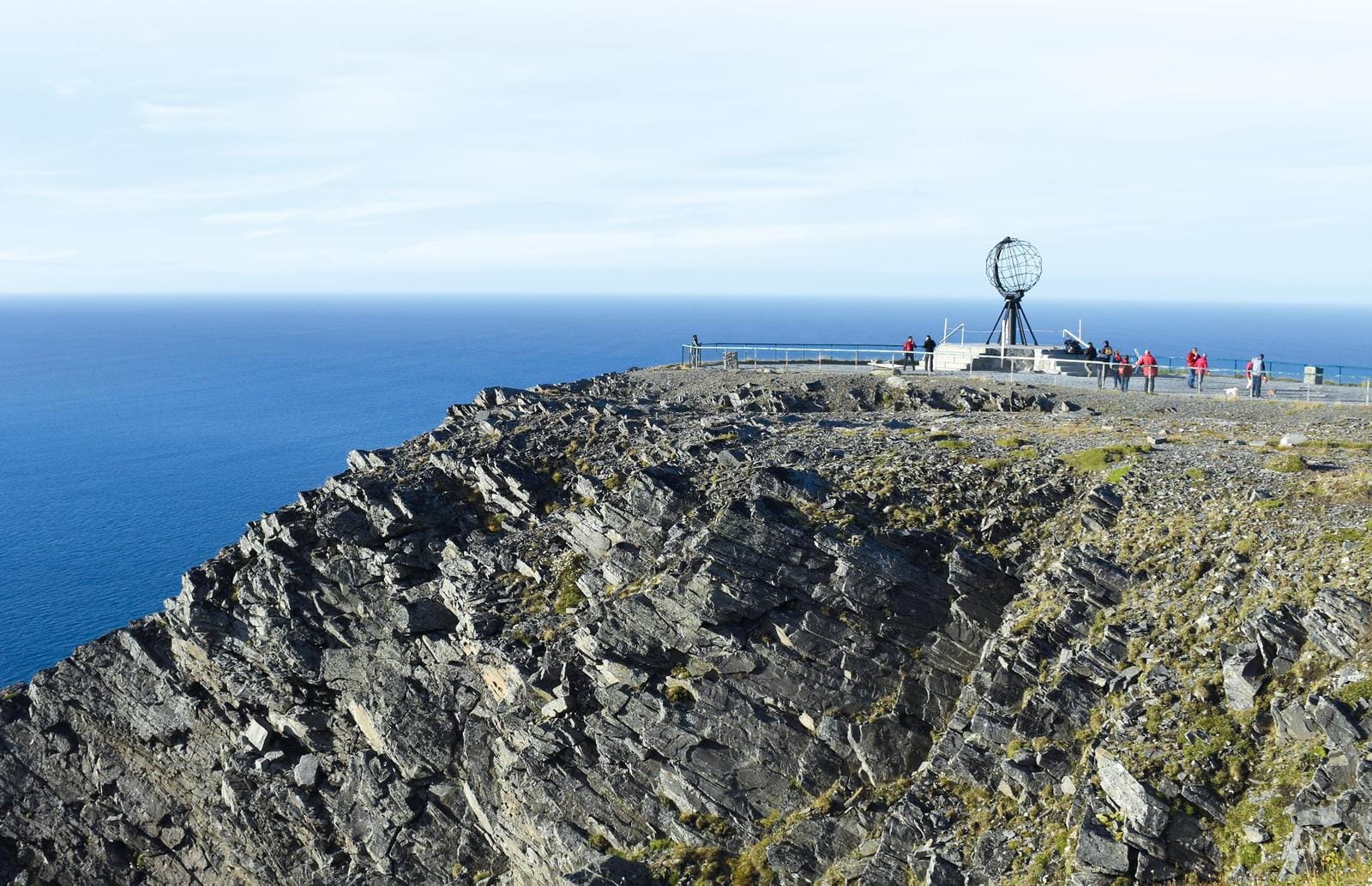 Nordkap, Norwegen: Felsige Klippen mit der Metallweltkugel und tiefblauem Meer im Hintergrund.
