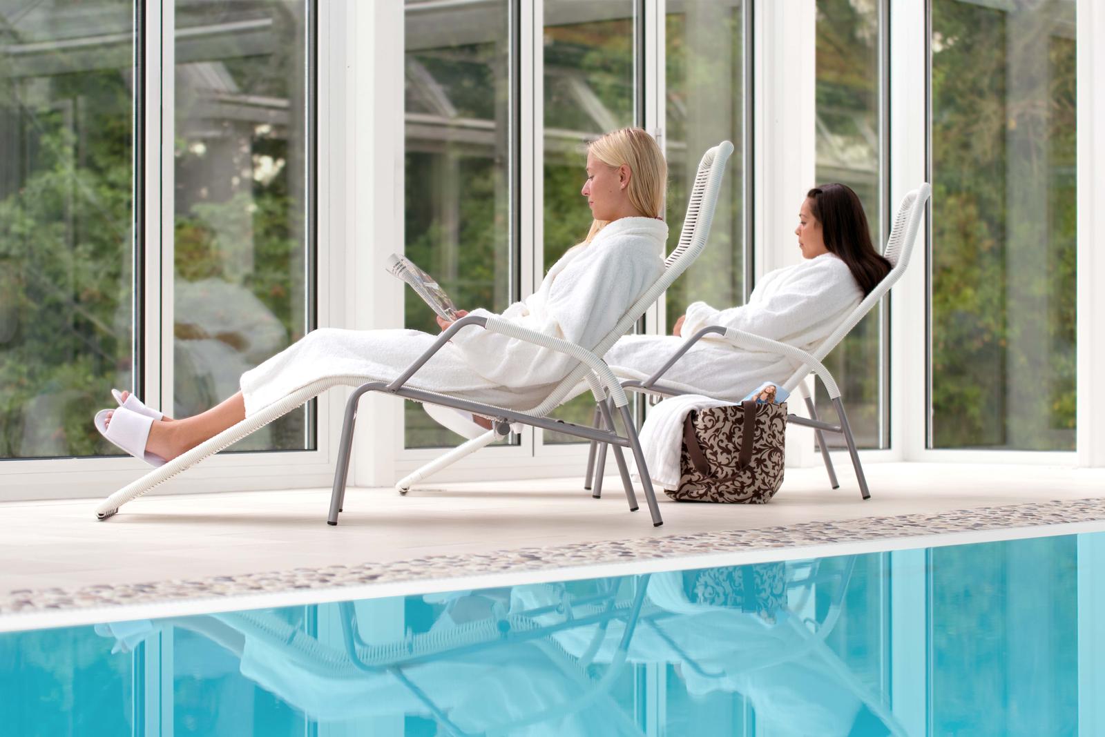 Zwei Personen entspannen in weißen Bademänteln am Pool in einem hellen Spa.
