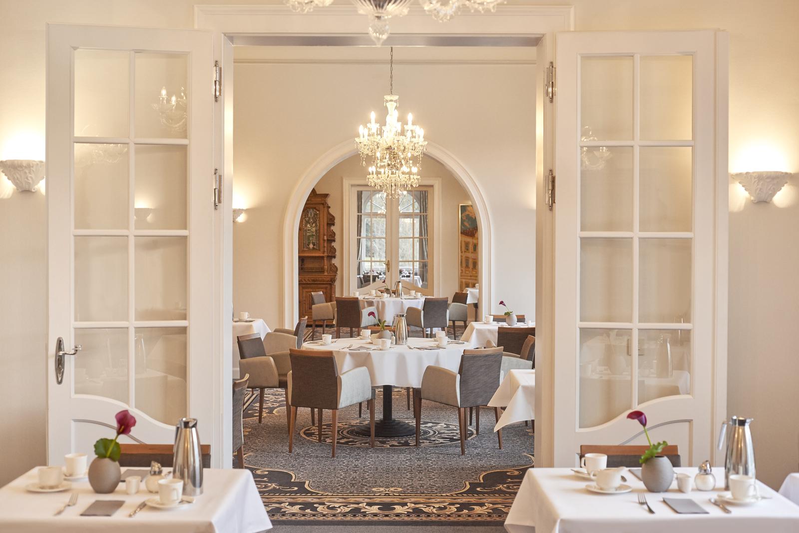 Elegantes Hotelrestaurant mit Kronleuchter, gedeckten Tischen und hellen Wänden.