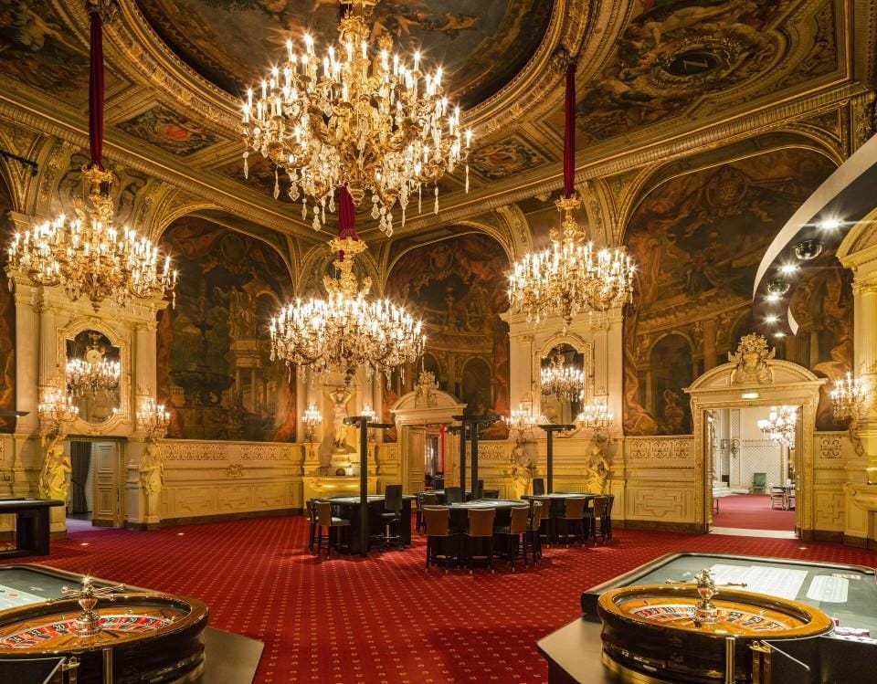 Prunkvolle Casinoräume mit Kronleuchtern und rotem Teppich; opulentes Ambiente.