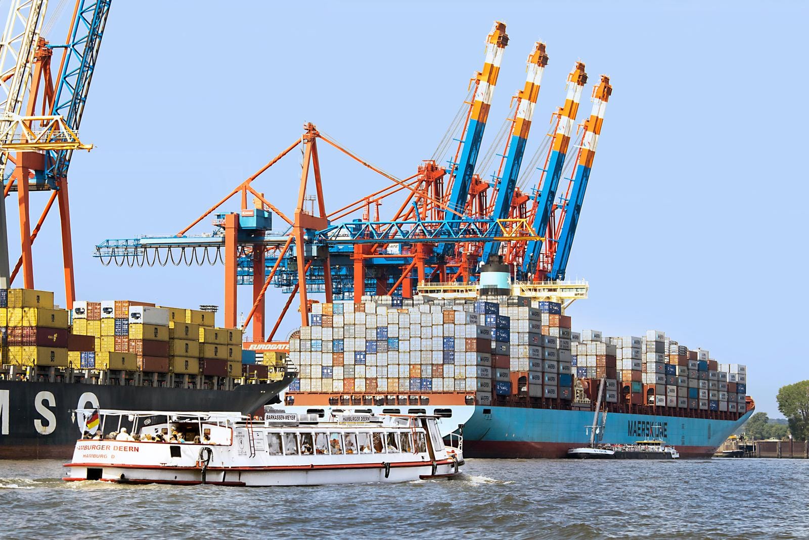 Containerschiff und Kräne im Hamburger Hafen unter blauem Himmel.