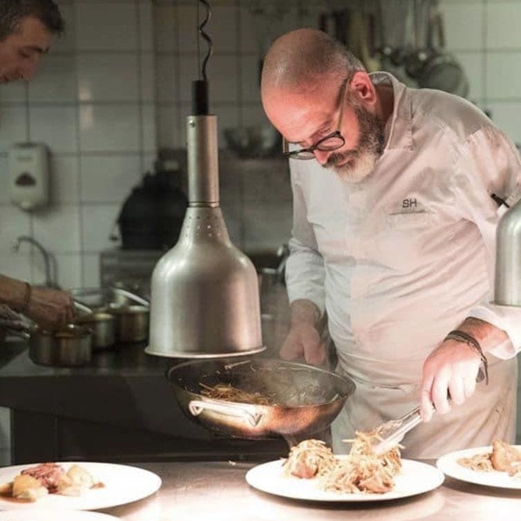 Ein Koch richtet unter warmer Beleuchtung Pasta in einer RestaurantkĂĽche an.