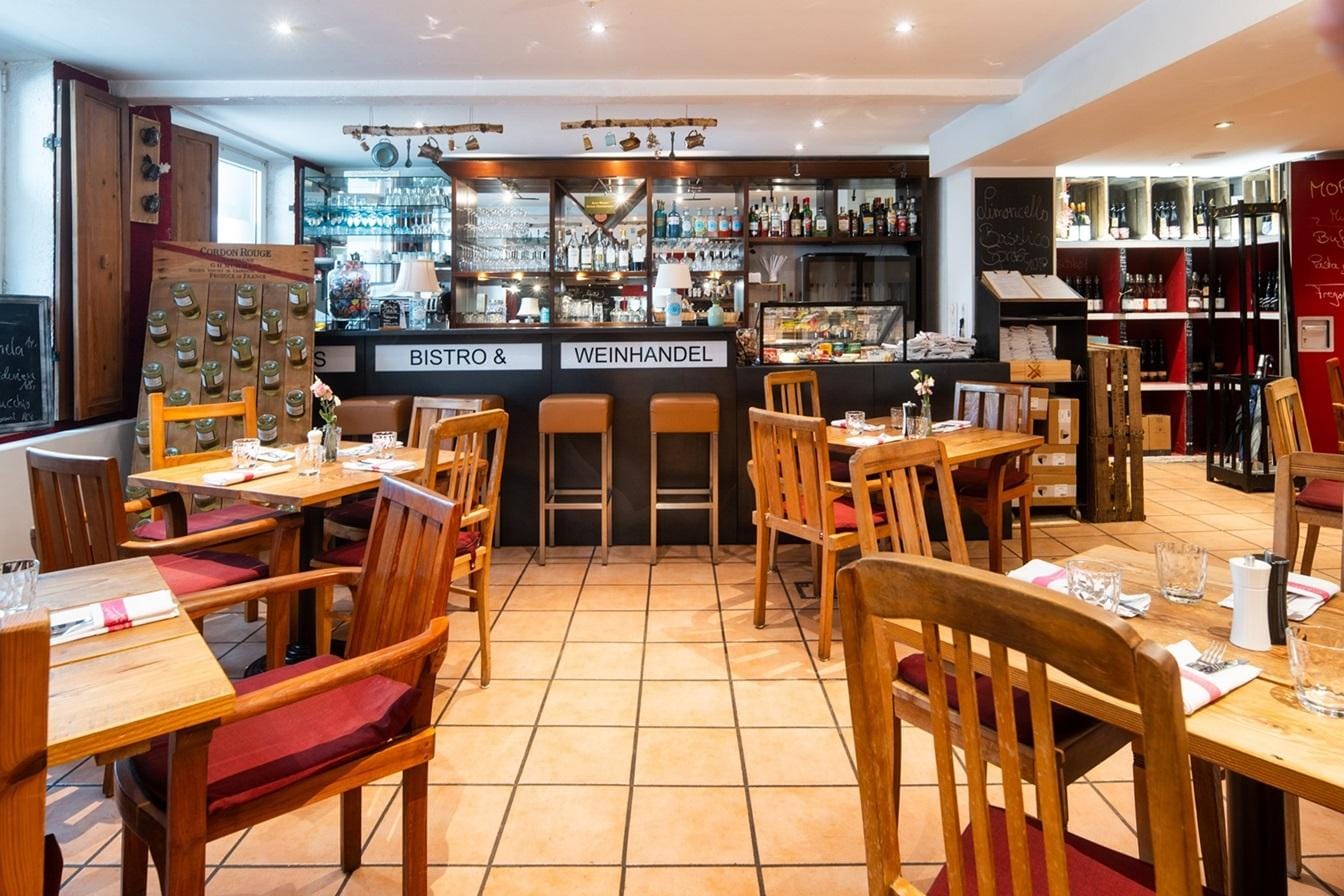 Gemütliches Bistro mit Holzmöbeln und gut bestücktem Weinhändler im Hintergrund.