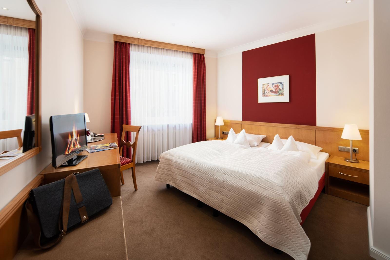 Gemütliches Hotelzimmer mit Doppelbett, Holzmöbeln, roter Akzentwand und Schreibtisch.
