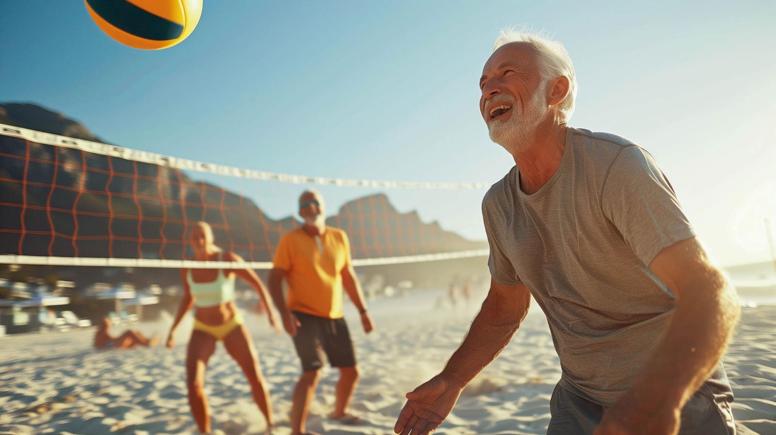 Strandvolleyballspiel bei Sonnenschein, Berge im Hintergrund, fröhliche Atmosphäre.