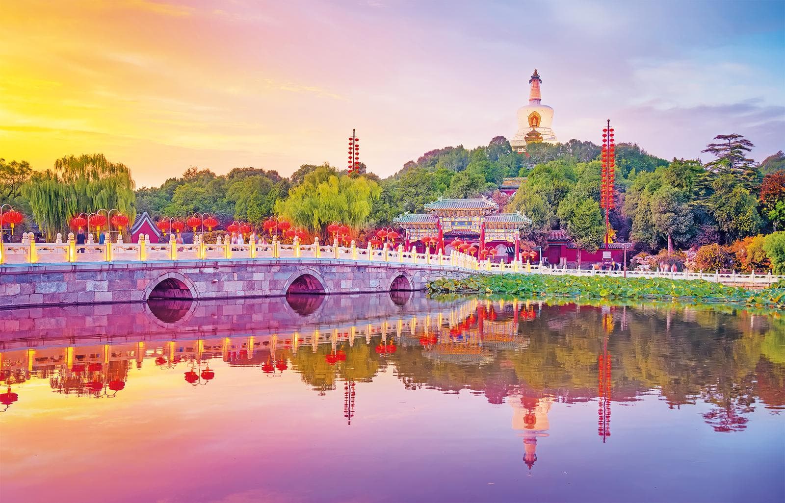 Bunt beleuchteter Pavillon und Brücke im Beihai-Park, Peking bei Sonnenuntergang.