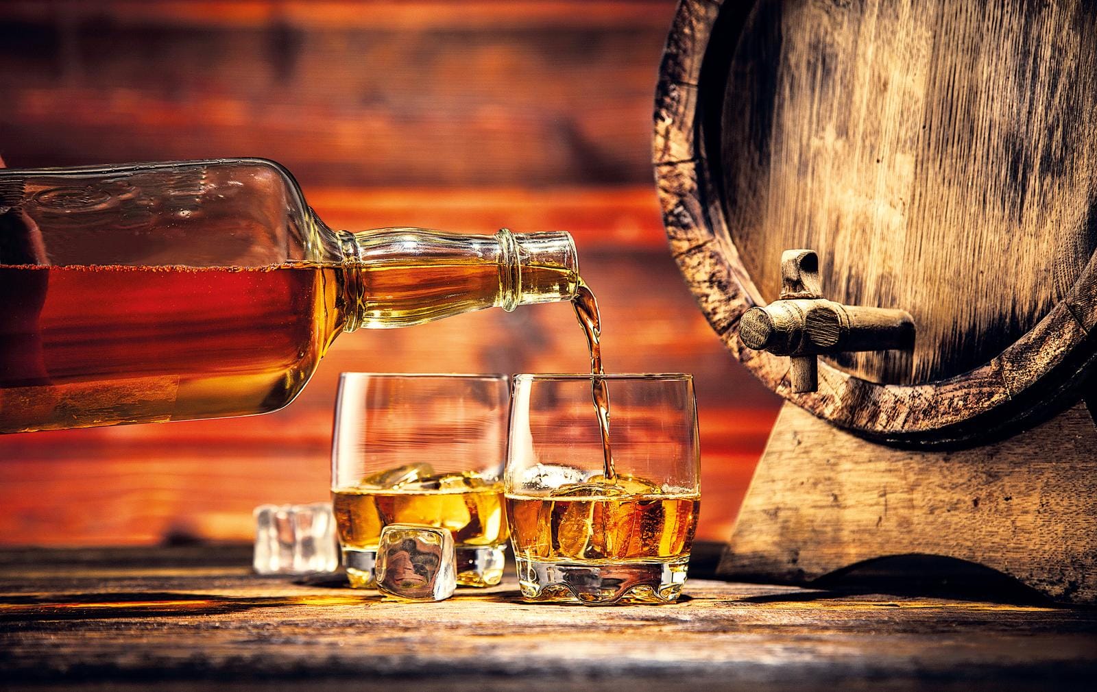 Whiskyflasche schenkt goldenen Whisky in Gläser neben Holzfass.