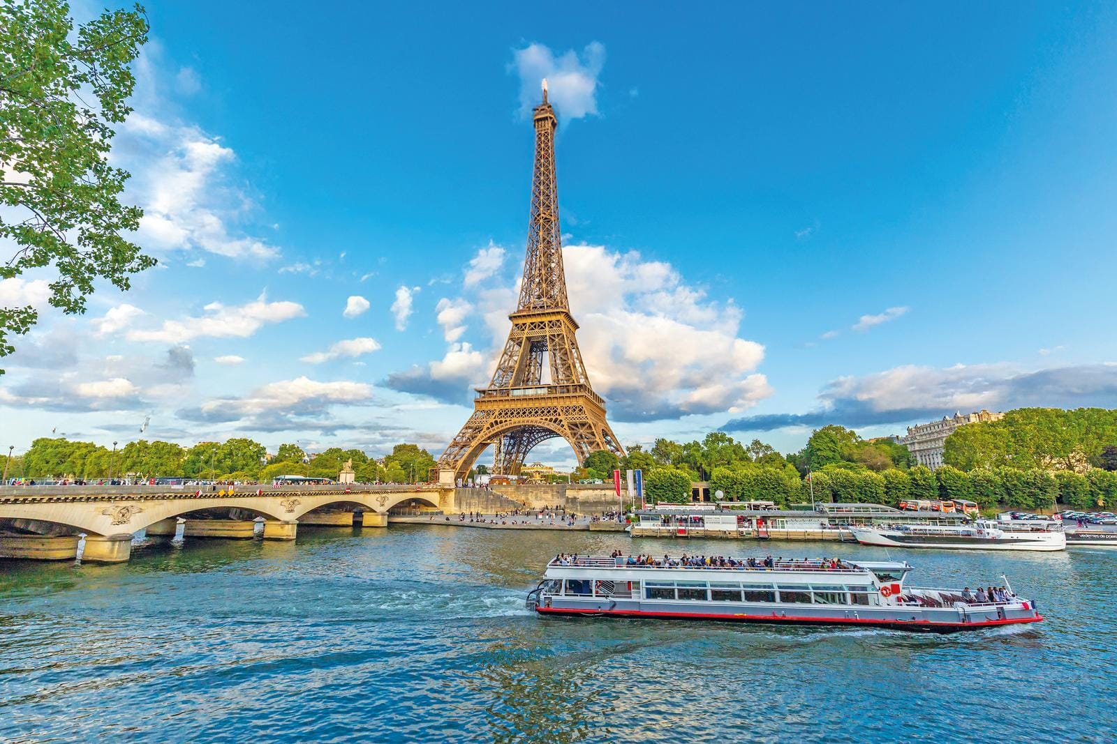 Eiffelturm in Paris, umgeben von blühenden Bäumen, blauem Himmel und Booten auf der Seine.
