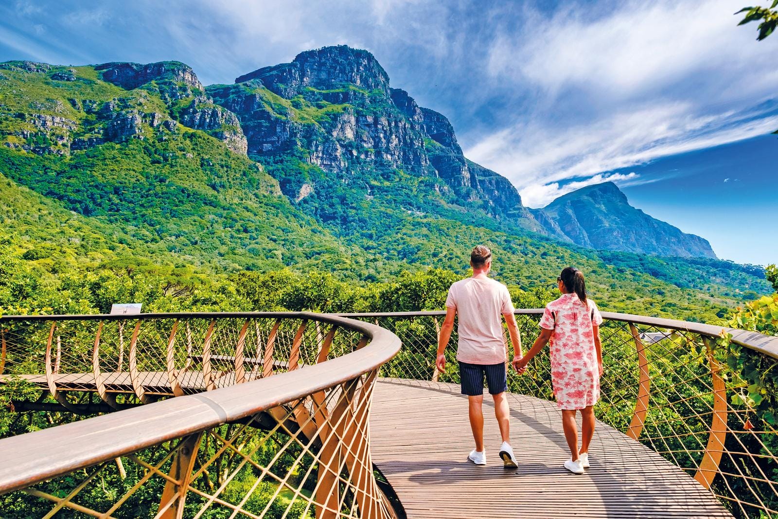 Paar auf Holzweg vor üppiger Berglandschaft im Kirstenbosch-Nationalpark, Südafrika.
