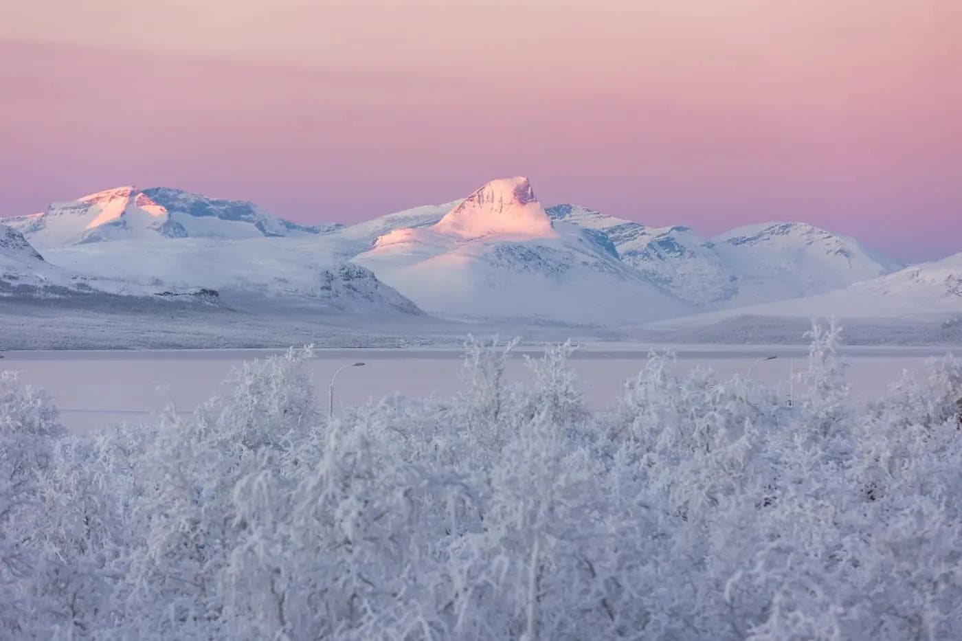 Verschneite Berge im Sonnenuntergang, Lappland, rosa Himmel, frostige Landschaft.