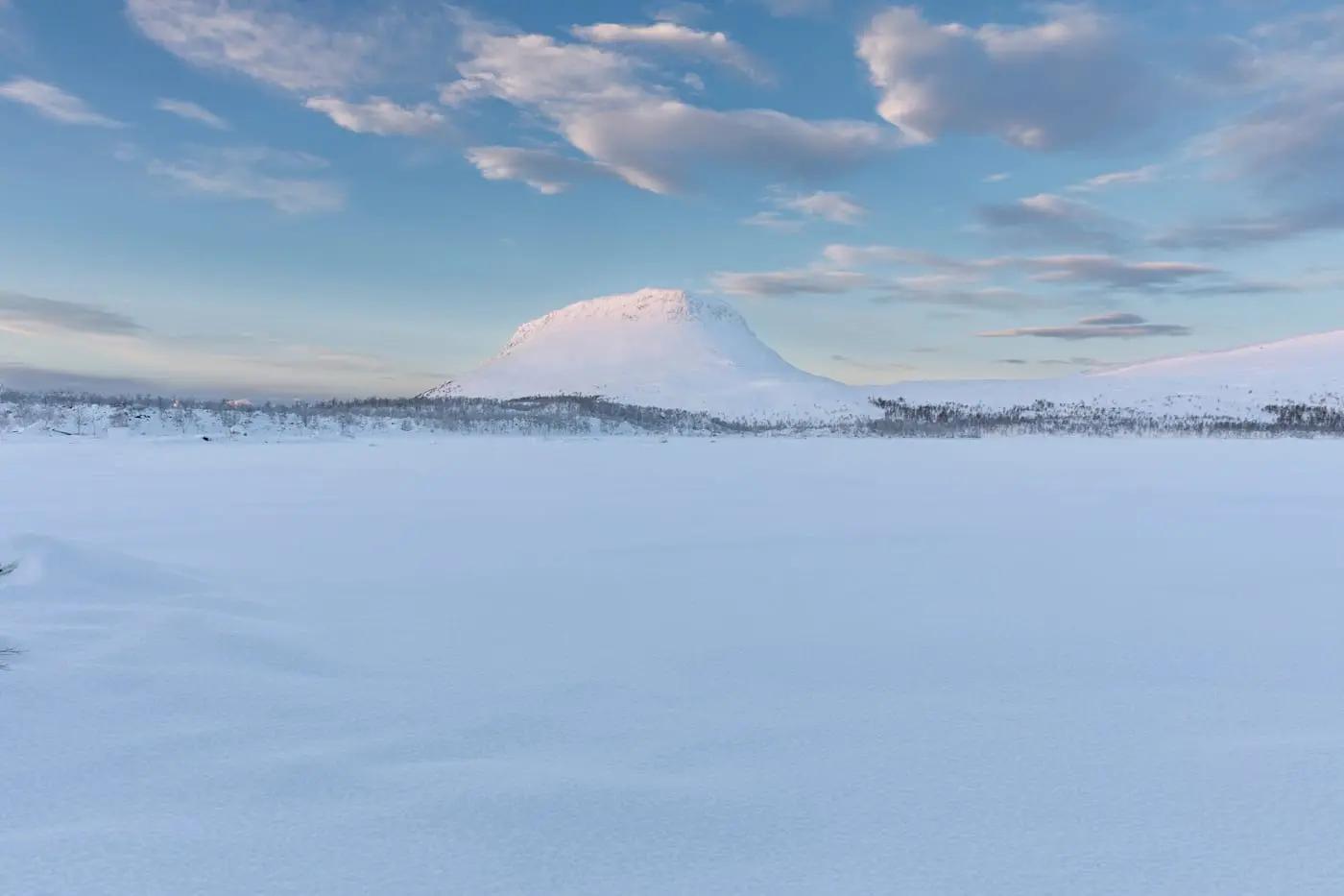 Verschneite Landschaft in Schweden mit Blick auf den Tunturi-Berg unter blauem Himmel.