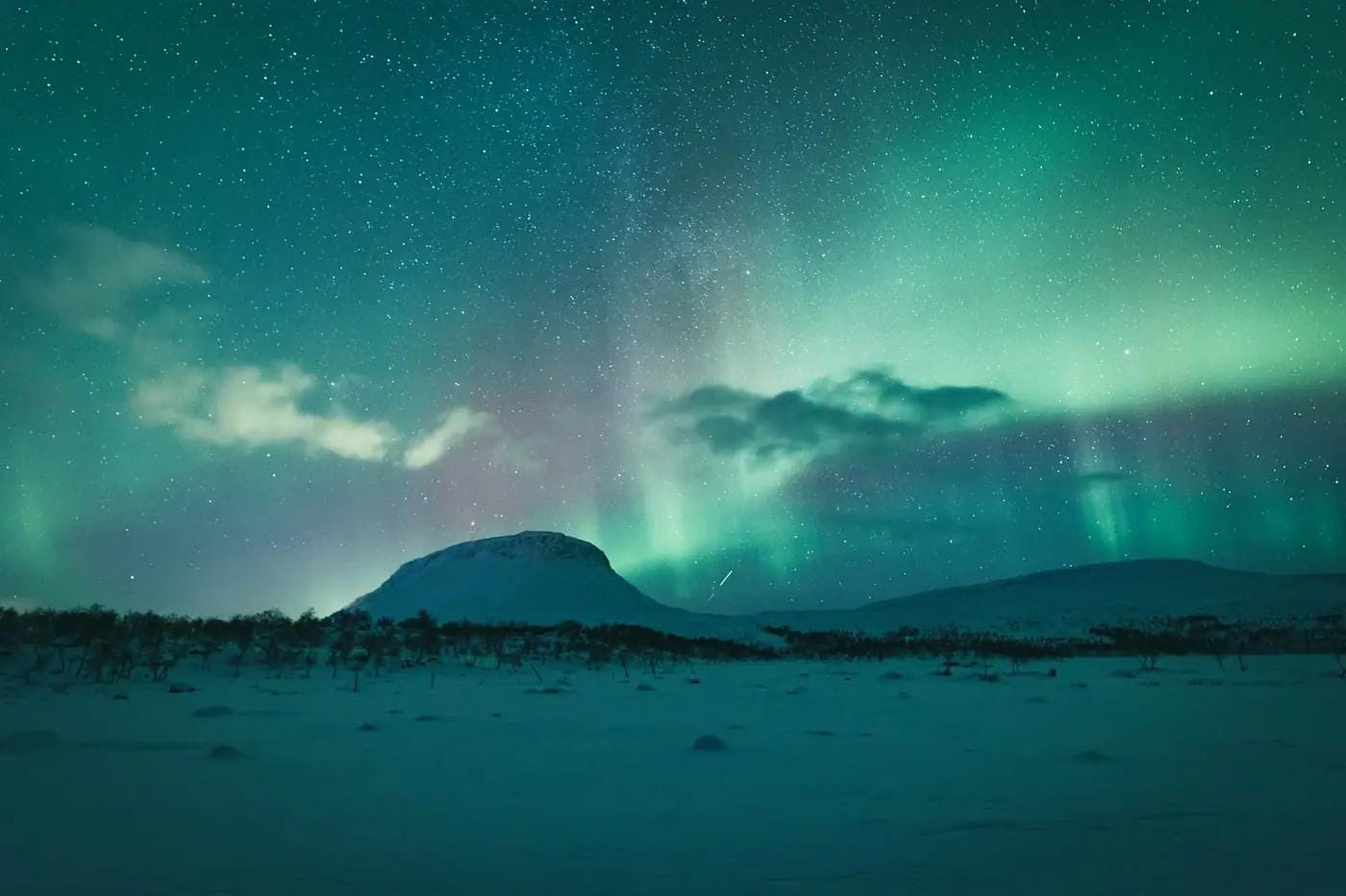 Polarlichter über verschneiter Landschaft, nächtlicher Himmel voller Sterne.