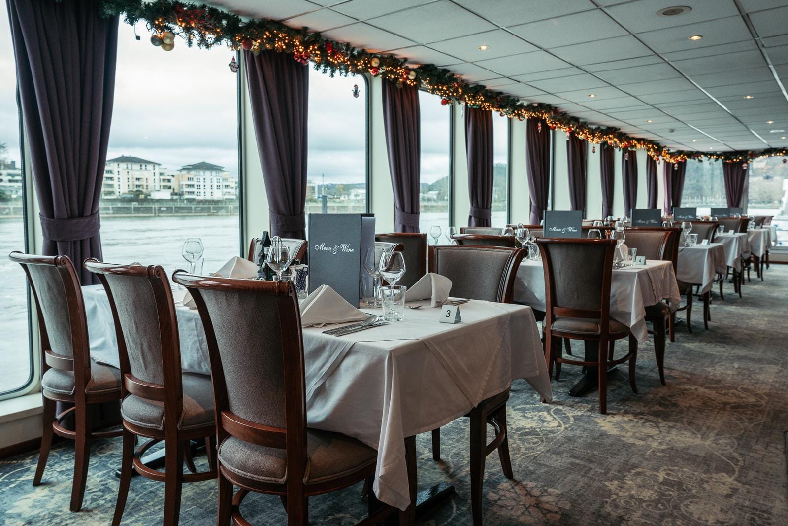 Elegantes Restaurant am Fluss mit festlicher Dekoration und Panoramafenstern.