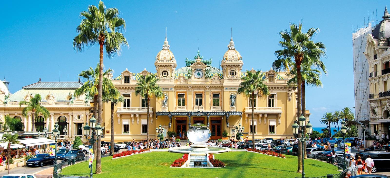 Prachtvolles Kasino in Monaco, umgeben von Palmen und lebendigem Treiben bei sonnigem Wetter.