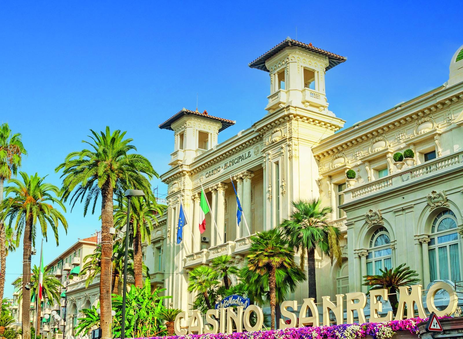 Historisches Casino in Sanremo, Italien, umgeben von Palmen und blühenden Pflanzen.